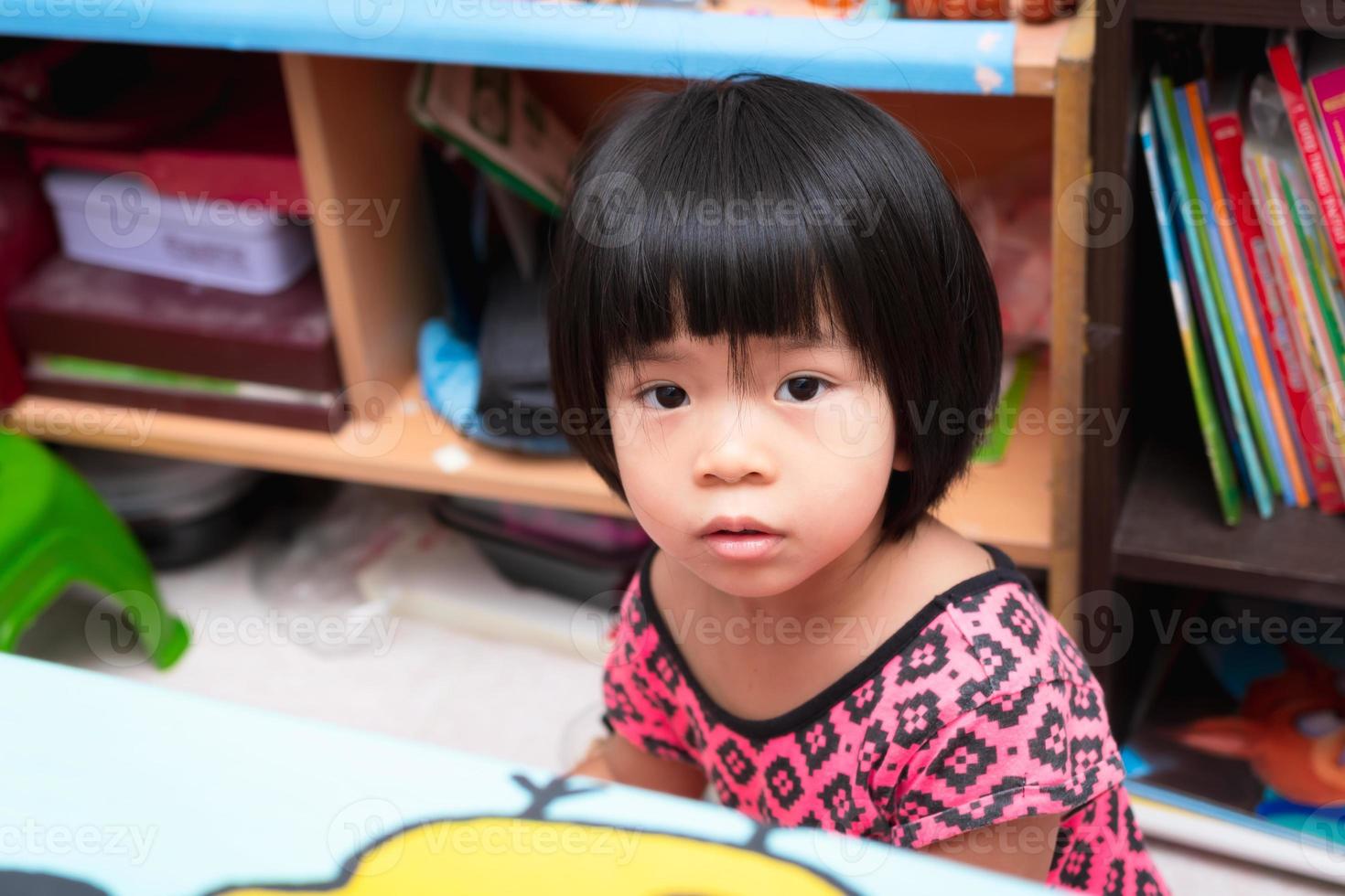 asiatico ragazzo ragazza è seduta nel un' disordinato camera. concetto di qualità di vita e raccolta giovane bambini. il corto dai capelli bambino è 4 anni vecchio. foto