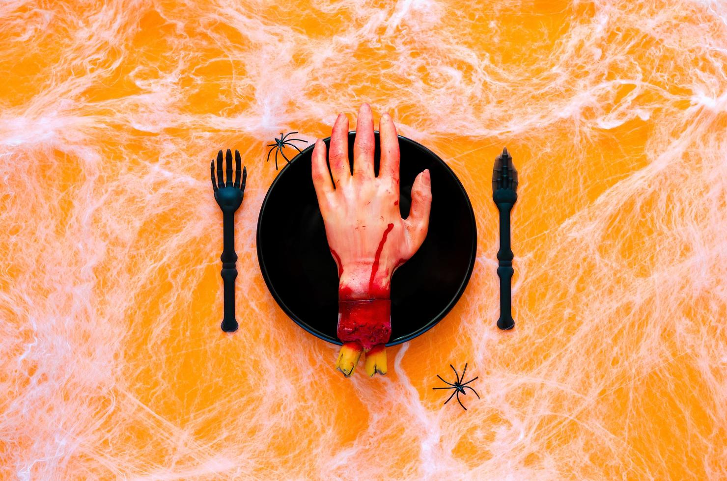 pauroso Halloween cena festa concetto con falso taglio mano su nero piatto, coltello e forchetta con ragno e ragnatela su arancia sfondo. foto