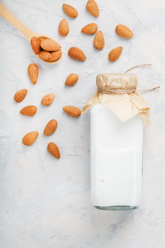 latte a partire dal biologico mandorle nel un' trasparente bottiglia con un' dispersione di semi e un' di legno cucchiaio su un' leggero sfondo foto