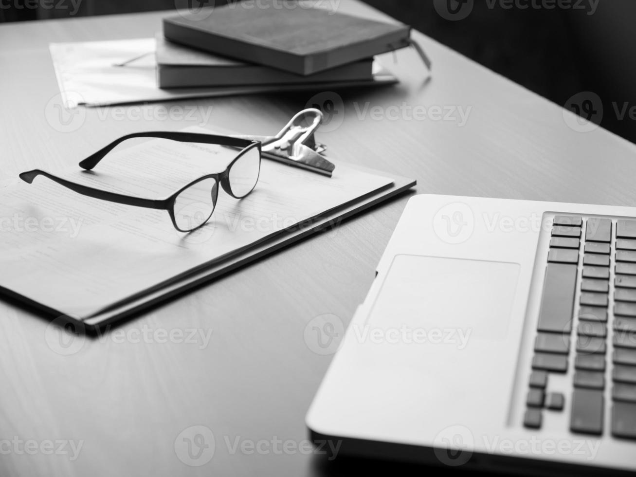 ufficio scrivania con computer portatile, occhiali, documenti e libro. nero e bianca tono foto