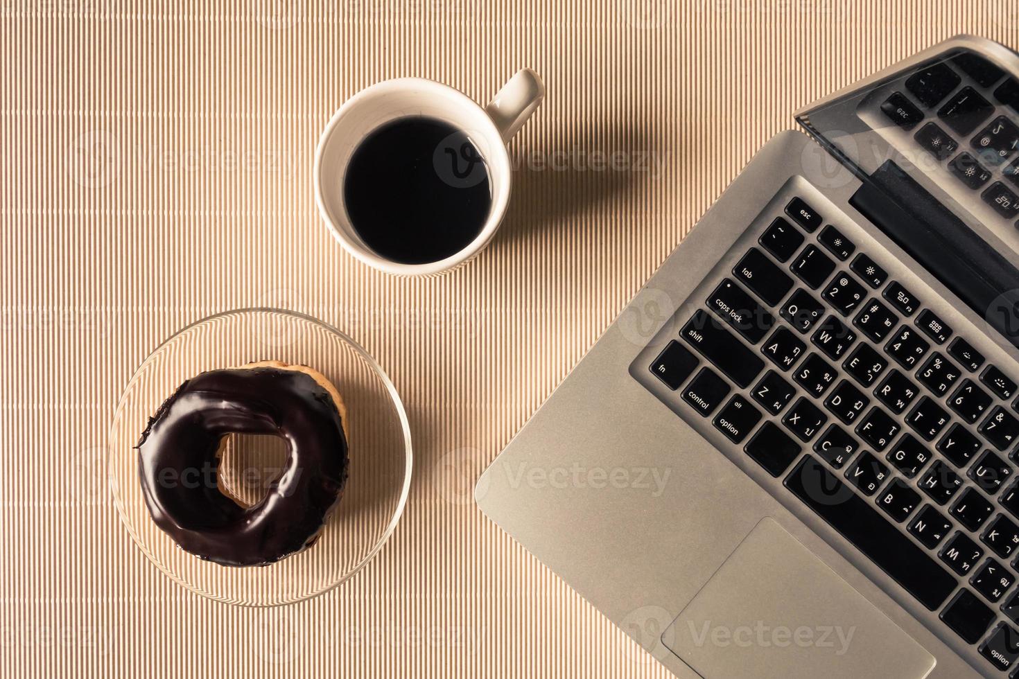 superiore Visualizza di il computer portatile con caffè tazza e ciambella su tavolo. foto