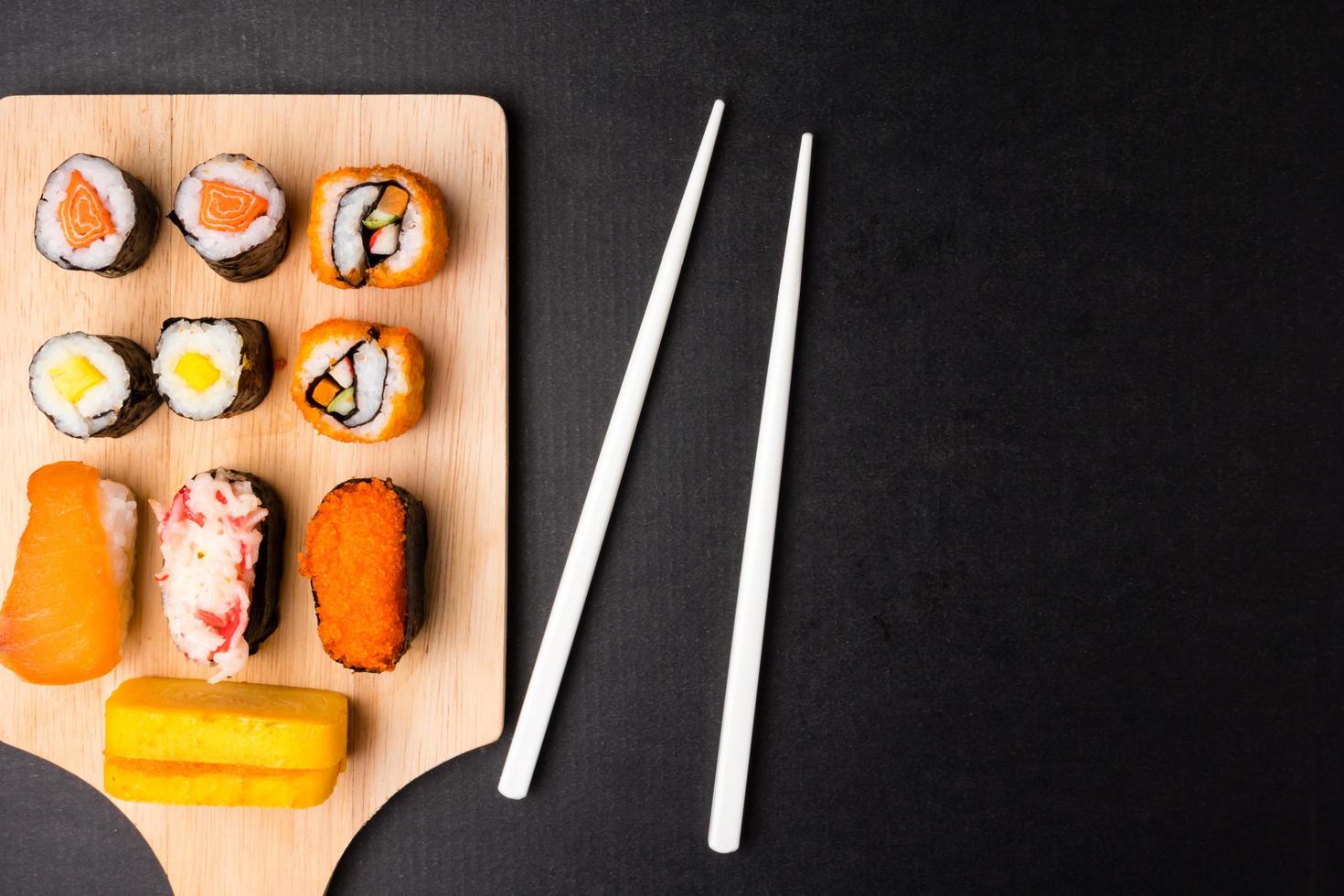 superiore Visualizza di Sushi impostato su di legno vassoio con bastoncini su nero sfondo, giapponese cibo. gratuito spazio per testo foto