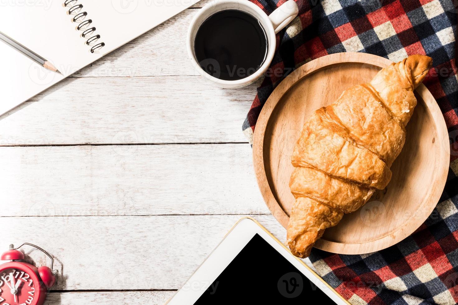 superiore Visualizza di brioche con caffè, tavoletta e taccuino su di legno tavolo sfondo. gratuito spazio per testo foto