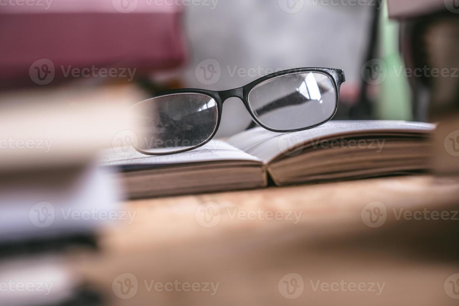 vicino su di Aperto libro con occhiali su di legno scrivania, morbido messa a fuoco. foto