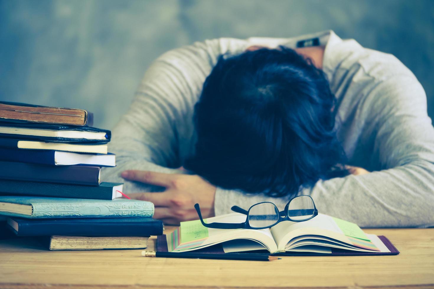 stanco giovane uomo addormentato con libro pile su il di legno tavolo. Vintage ▾ tono foto