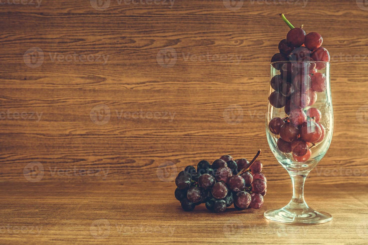 rosso uva nel bicchiere su il di legno tavolo. gratuito spazio per testo foto