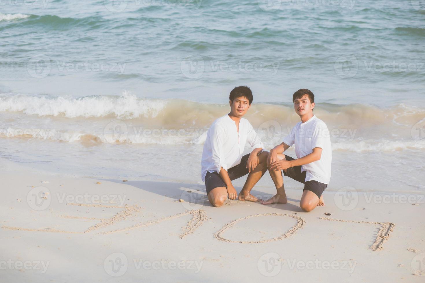 giovane coppia asiatica gay sorridente disegno romantico parola testo amore insieme sulla sabbia in vacanza, omosessuale felice e divertente con amore seduto sulla sabbia in spiaggia in viaggio estate, concetto legale lgbt. foto