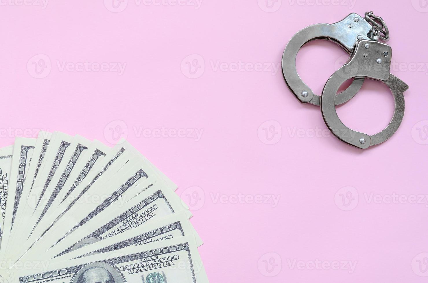 manette della polizia e centinaia di dollari americani giacciono su uno sfondo rosa foto