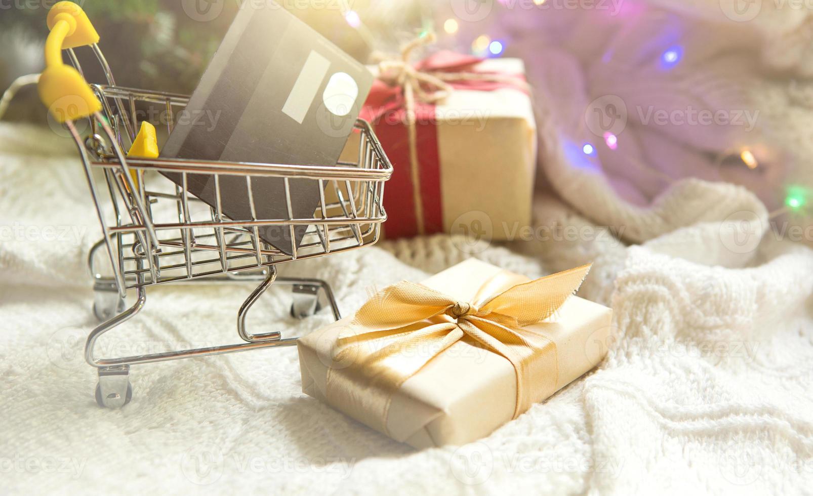 scatola con un' regalo nel Natale confezione nel shopping carrello su bianca a maglia lenzuolo. nero venerdì, acquisto i regali per nuovo anno. vacanza arredamento, banca plastica carta - senza soldi pagamento, in linea negozio. copia spazio foto