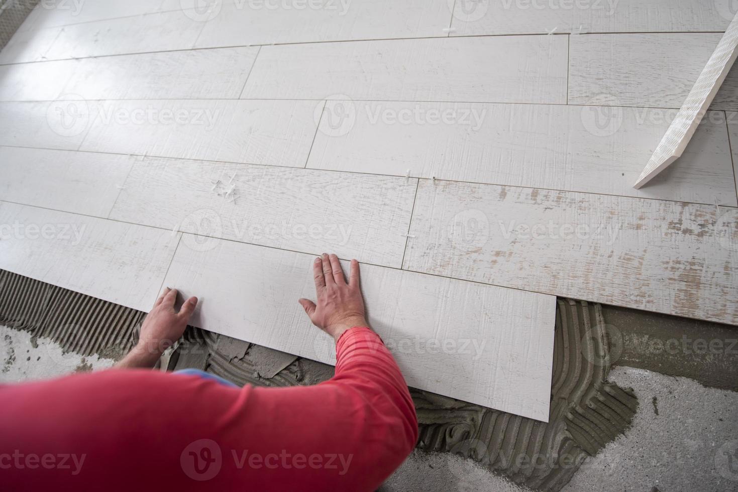 operaio che posa le piastrelle in ceramica effetto legno sul pavimento foto