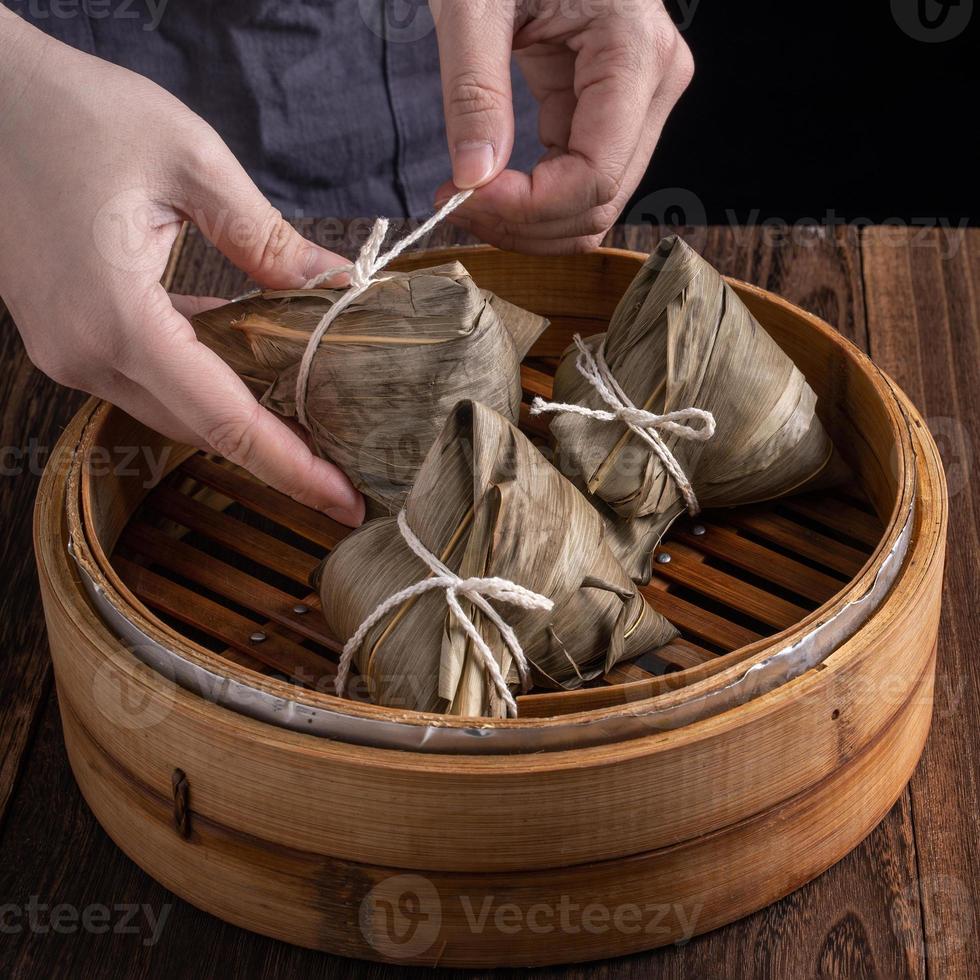 gnocco di riso, zongzi - festival della barca del drago, mazzetto di cibo cucinato tradizionale cinese nel piroscafo su tavola di legno su sfondo nero, primo piano, spazio di copia foto
