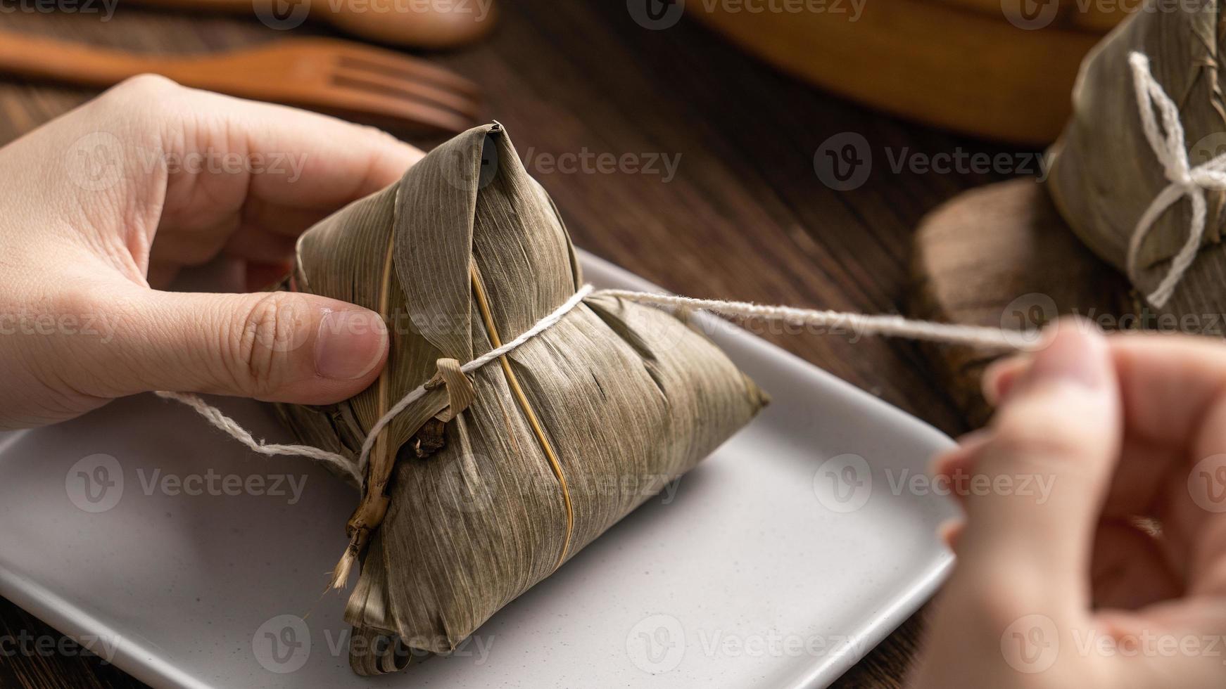 Drago barca Festival cibo - riso gnocco zongzi, giovane asiatico donna mangiare Cinese tradizionale cibo su di legno tavolo a casa celebrazione, vicino su foto