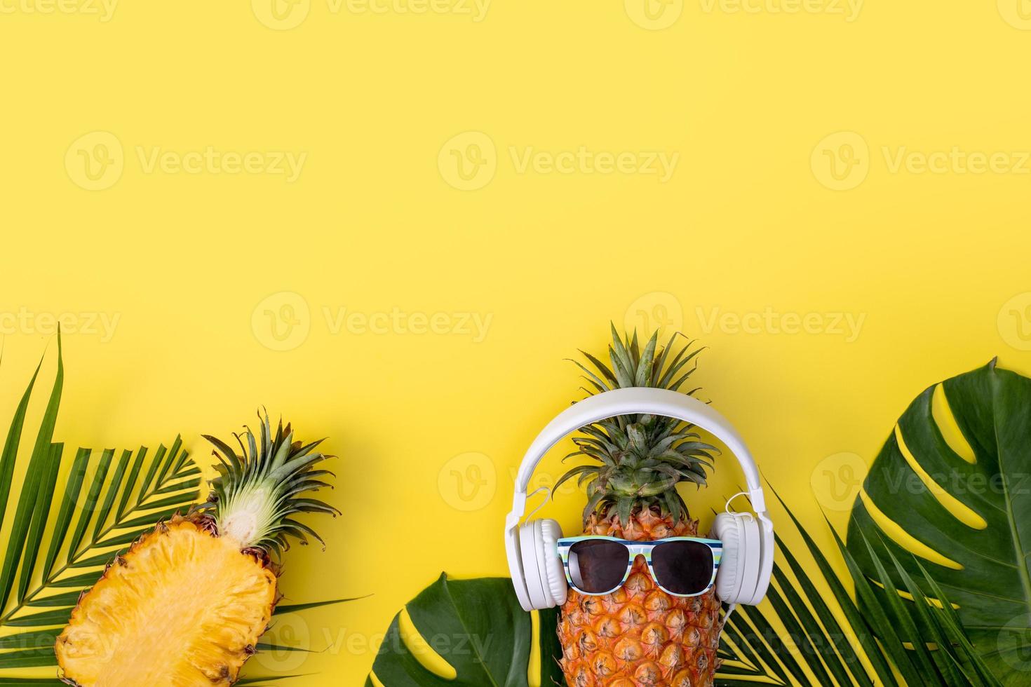 divertente ananas che indossa una cuffia bianca, ascolta musica, isolata su sfondo giallo con foglie di palma tropicali, vista dall'alto, concetto di design piatto. foto