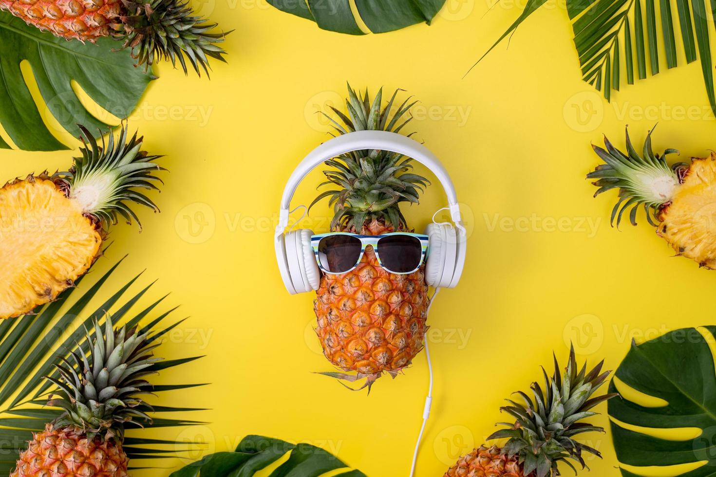 divertente ananas che indossa una cuffia bianca, ascolta musica, isolata su sfondo giallo con foglie di palma tropicali, vista dall'alto, concetto di design piatto. foto