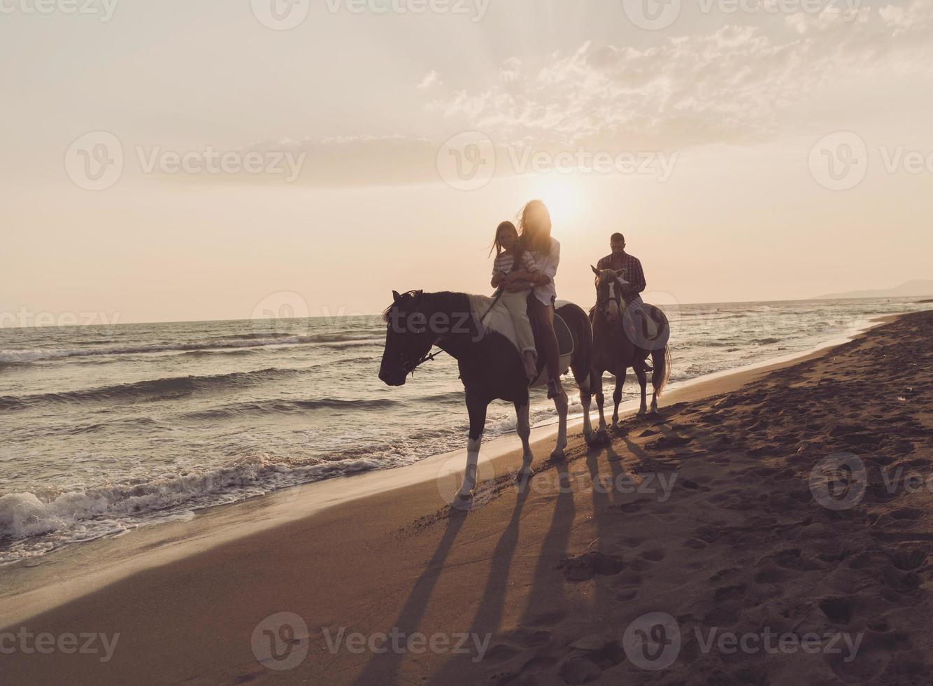 il famiglia spende tempo con loro bambini mentre equitazione cavalli insieme su un' bellissimo sabbioso spiaggia su tramonto. foto