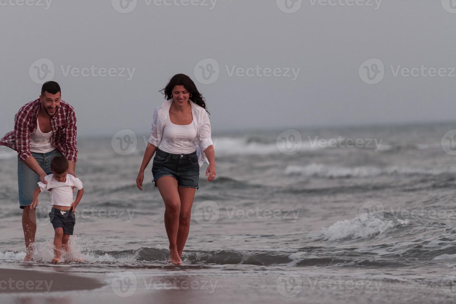 il famiglia gode loro vacanza come essi camminare il sabbioso spiaggia con loro figlio. selettivo messa a fuoco foto