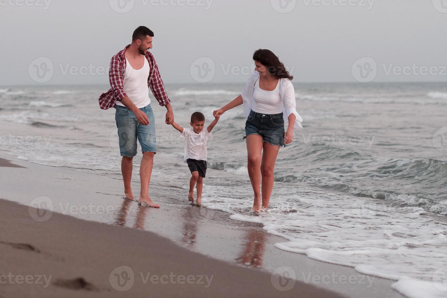 il famiglia gode loro vacanza come essi camminare il sabbioso spiaggia con loro figlio. selettivo messa a fuoco foto