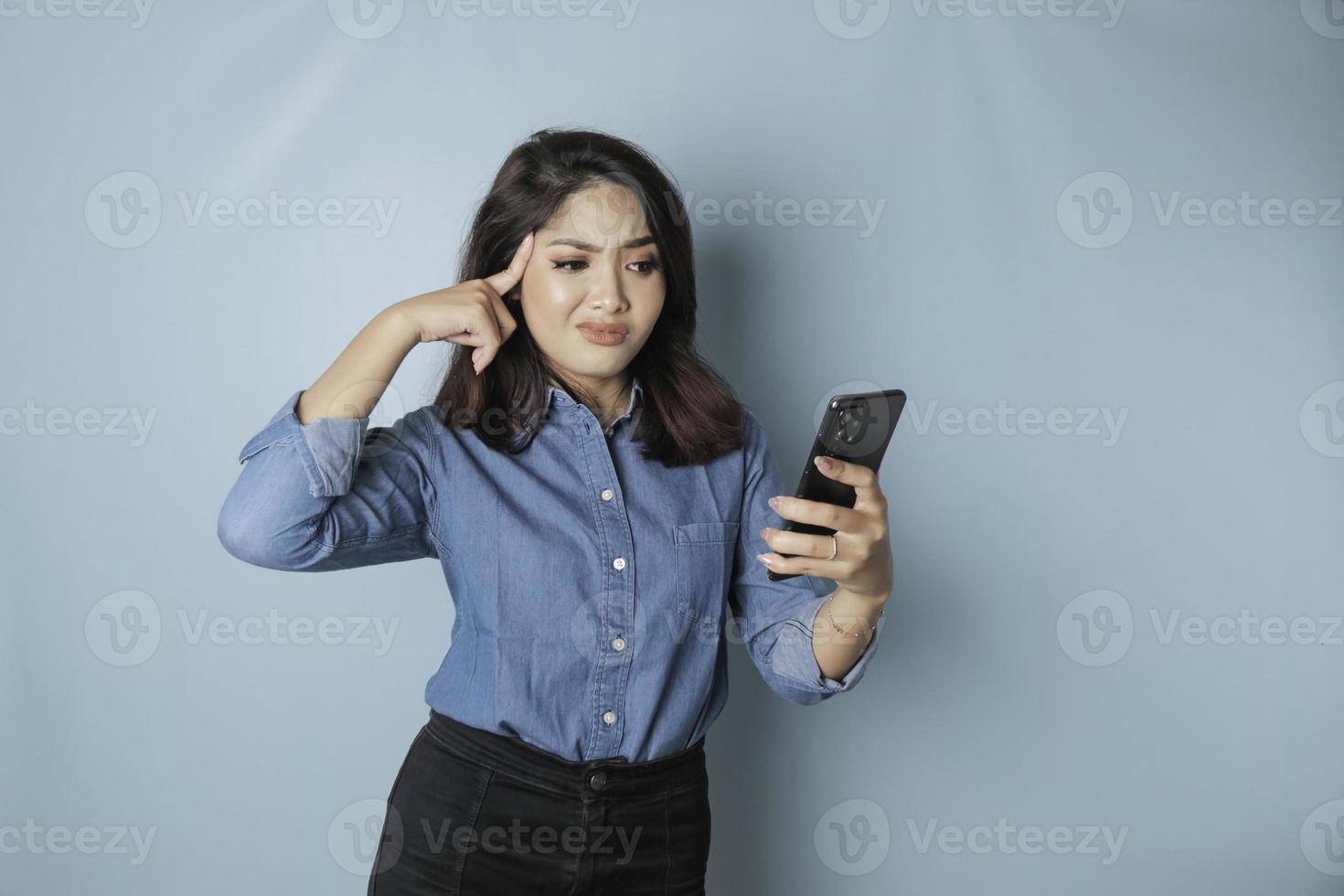 stanco pensiero donna, ha un' triste espressione mentre Tenere sua smartphone. isolato blu sfondo foto