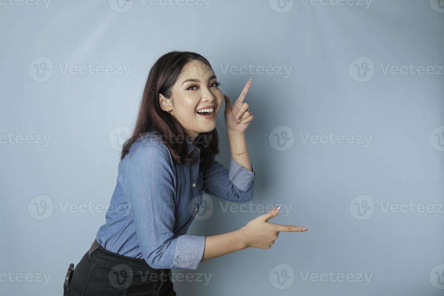 eccitato asiatico donna indossare blu camicia puntamento a il copia spazio accanto suo, isolato di blu sfondo foto