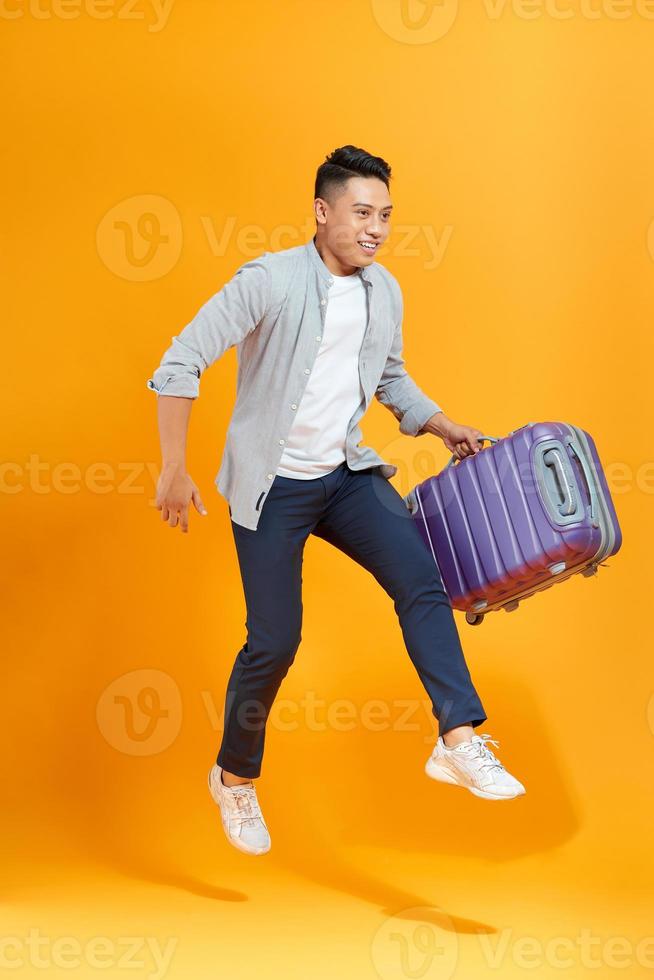 attraente contento giovane asiatico uomo turista con aria biglietto e passaporto nel il suo mano salto isolato su giallo studio sfondo foto