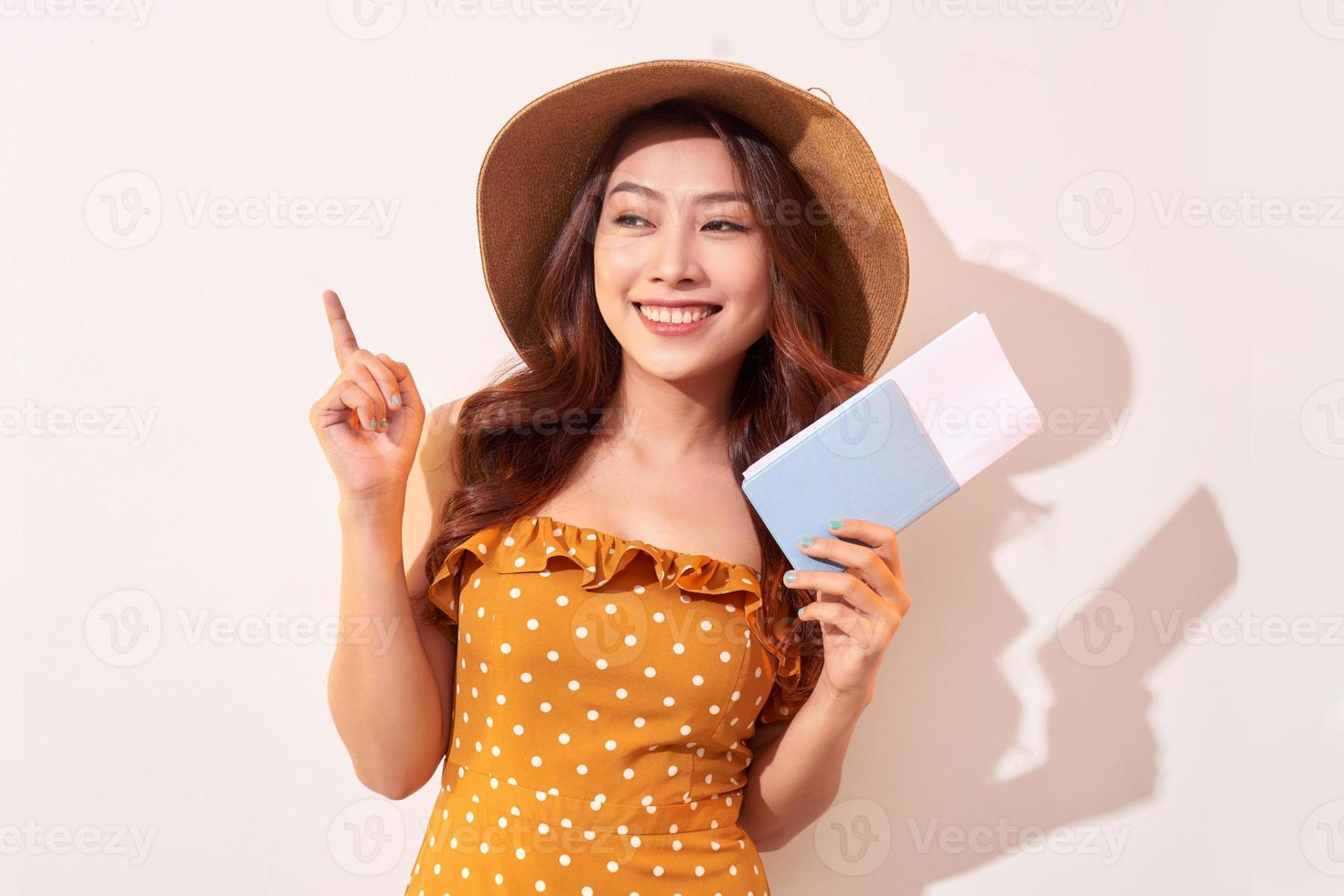 un' giovane donna nel un' arancia polka puntini vestito con un' cannuccia cappello su sua testa è Tenere un' passaporto e aereo Biglietti foto