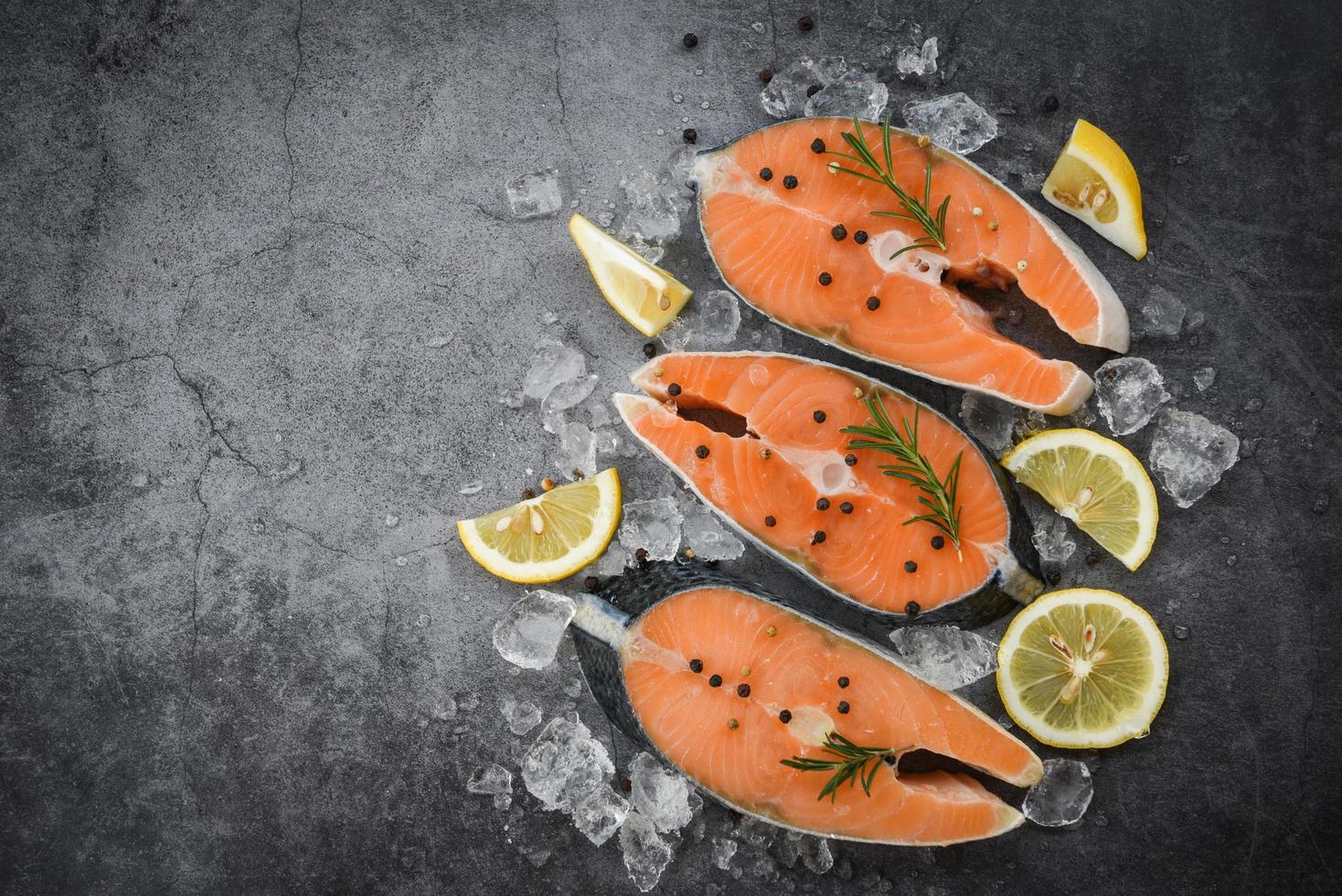 trancio di salmone fresco con erbe e spezie limone rosmarino su sfondo piatto nero salmone crudo filetto di pesce e ghiaccio per bistecca cotta di frutti di mare foto