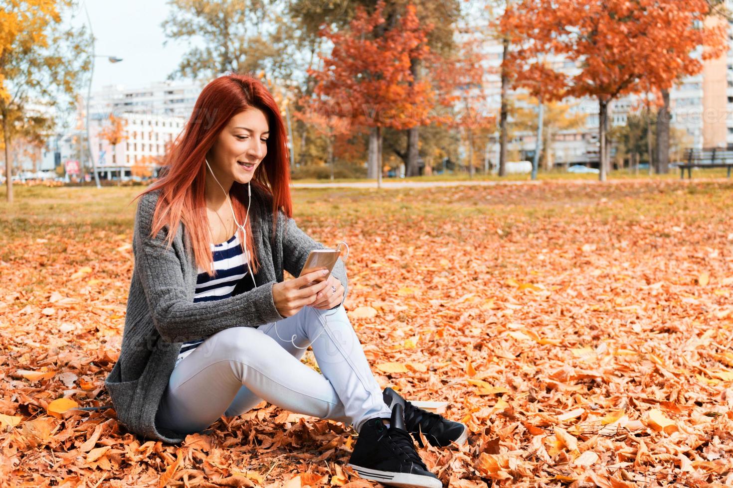 contento testa Rossa donna utilizzando mobile Telefono nel autunno parco. foto