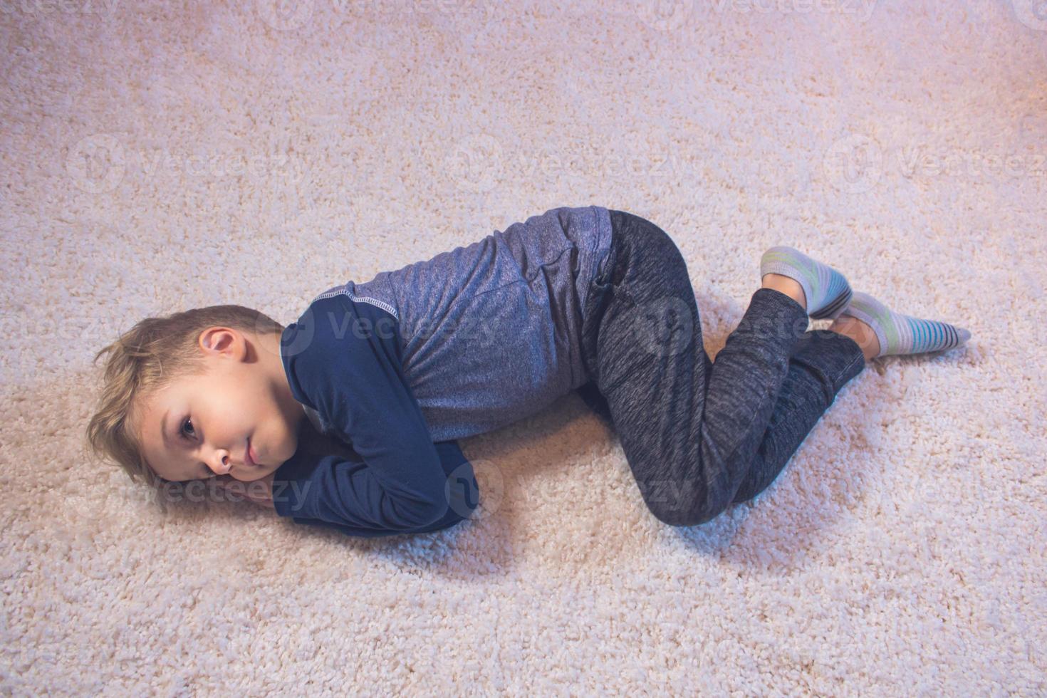 piccolo ragazzo rilassante mentre dire bugie giù su tappeto a casa foto