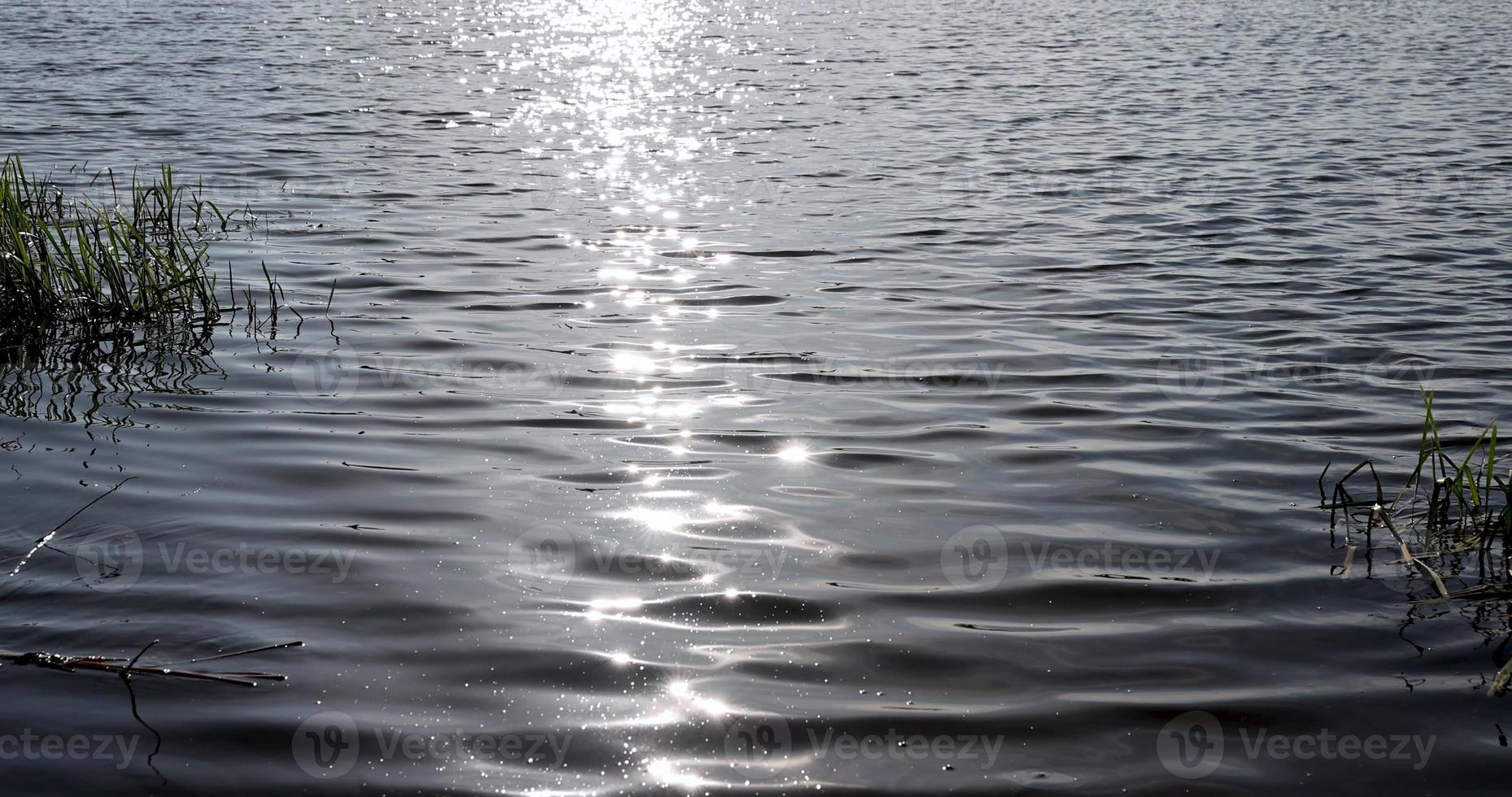 bagliore di luce del sole su il superficie di il lago acqua con piccolo onde foto