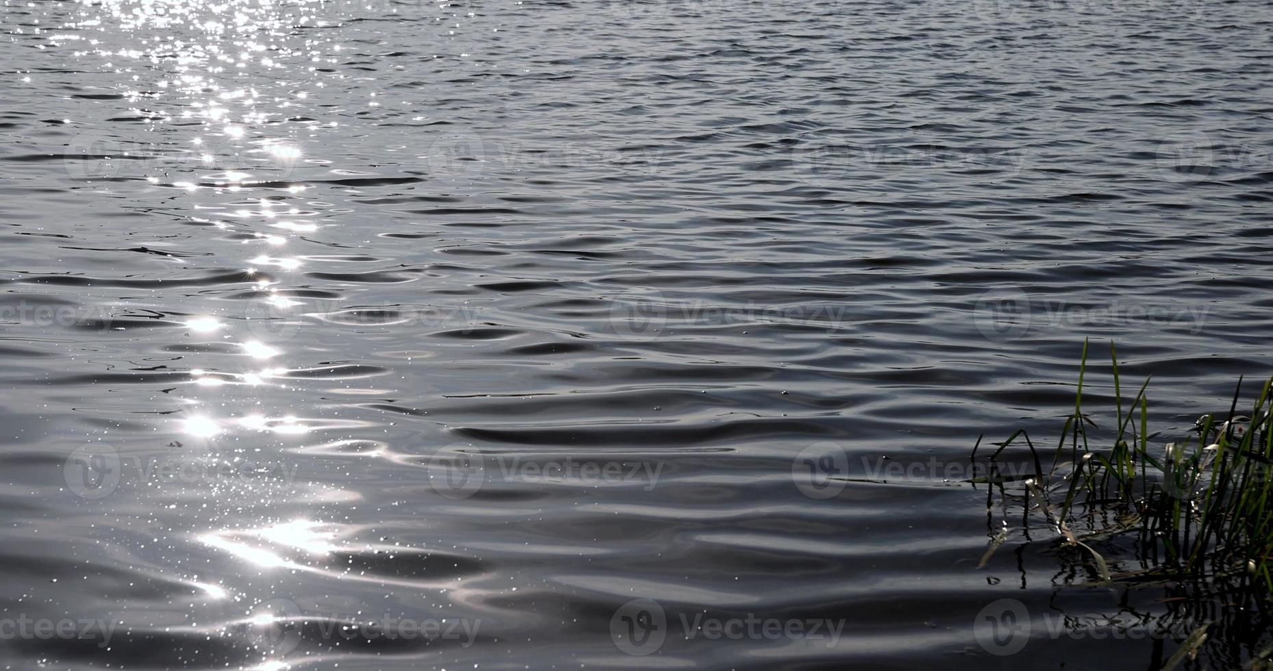 bagliore di luce del sole su il superficie di il lago acqua con piccolo onde foto