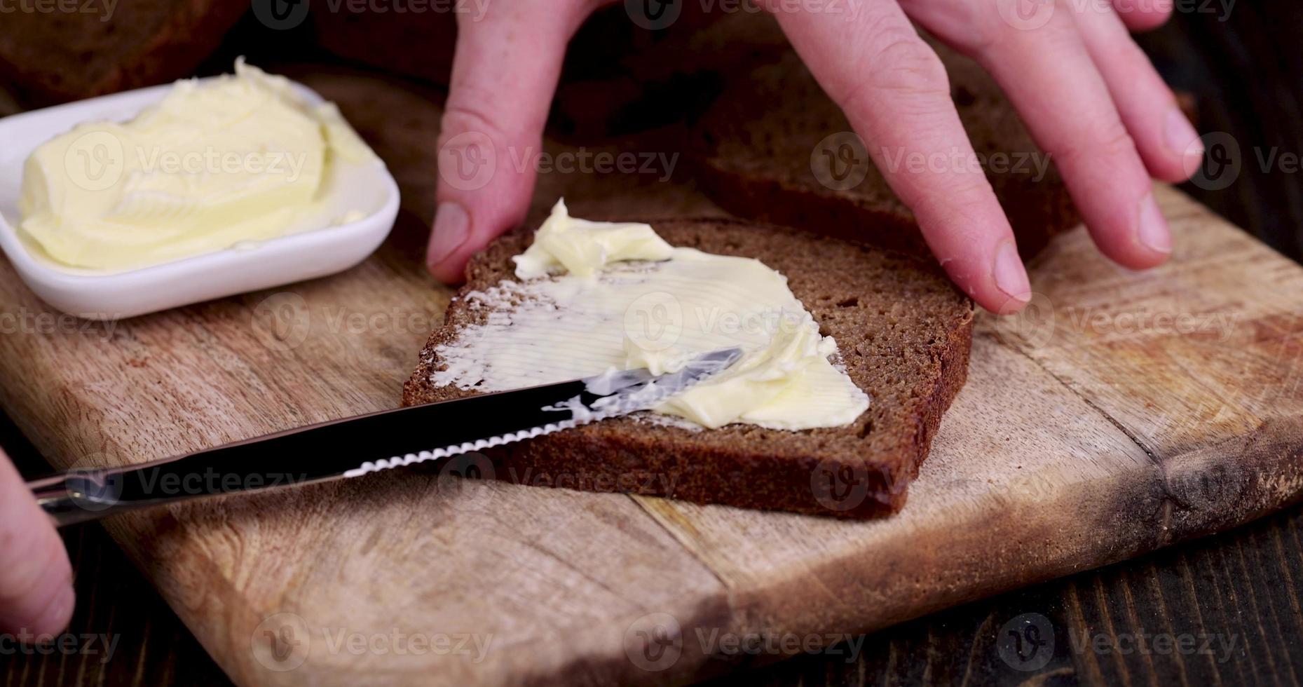 spalmare il burro di latte sul pane nero di segale foto