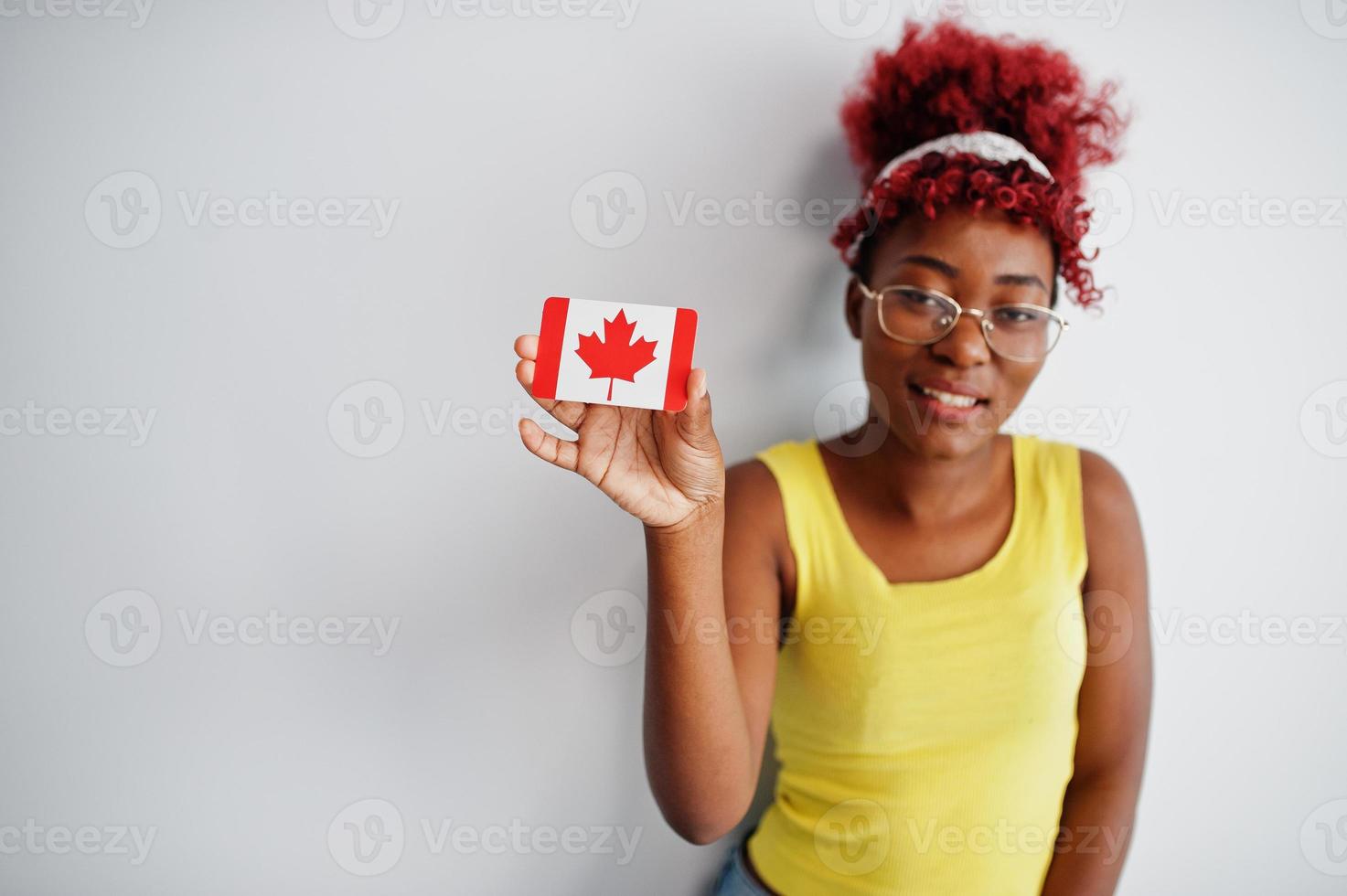 africano americano donna con afro capelli, indossare giallo canottiera e occhiali, hold Canada bandiera isolato su bianca sfondo. foto