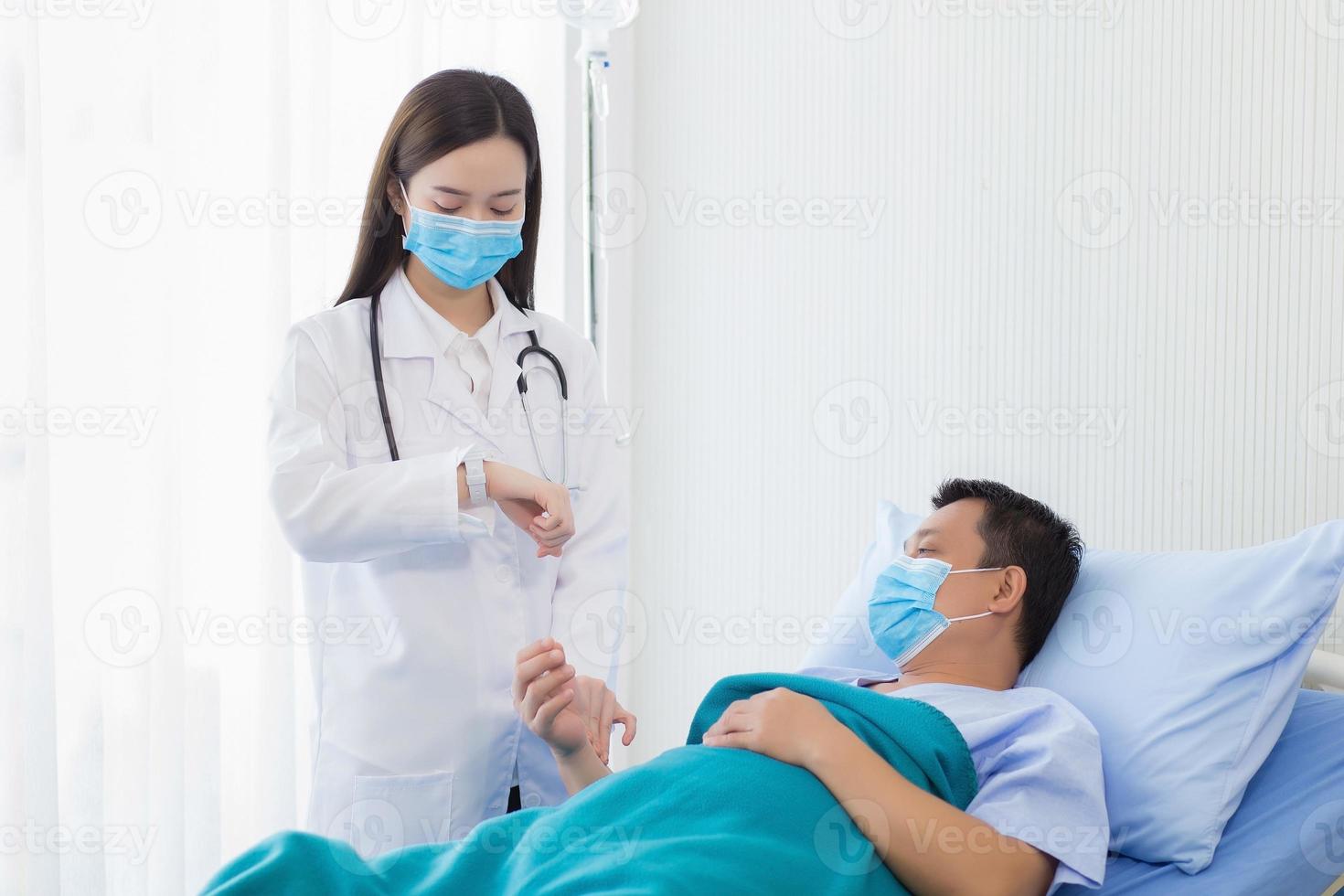 un asiatico donna medico è assunzione il pulse su il polso di un' uomo paziente chi lui è su letto di il suo dolore e sintomo nel ospedale foto