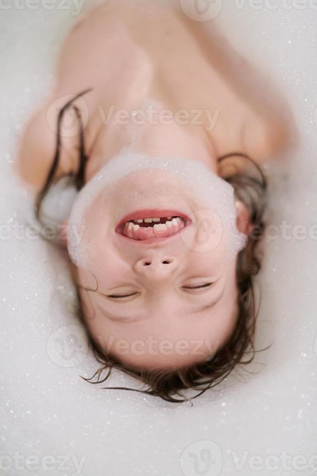 poco ragazza nel bagno giocando con sapone schiuma foto