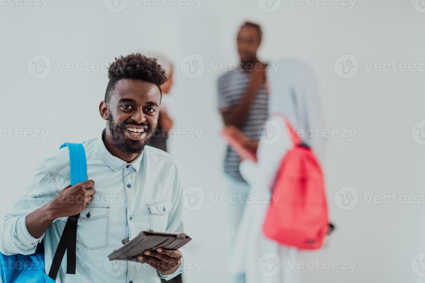 Università stile di vita alunno Tenere un' tavoletta computer e sorridente mentre in piedi contro Università con il suo amici avere un' squadra incontro nel il sfondo. alta qualità foto