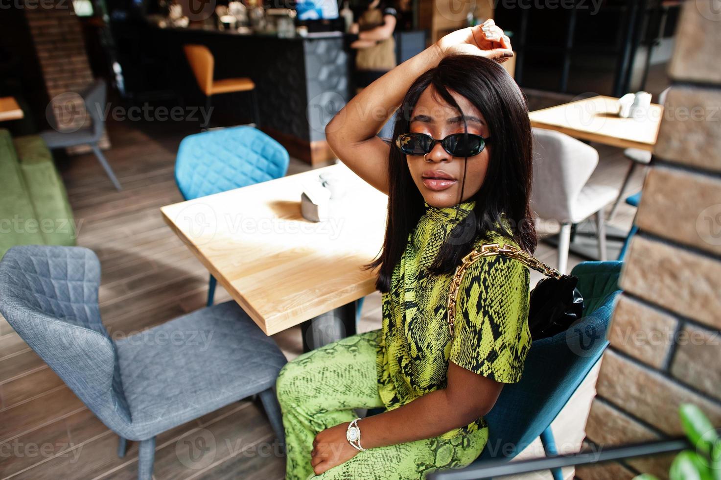 fascino africano americano donna indossare alla moda serpente vestito e occhiali da sole posa a ristorante. foto