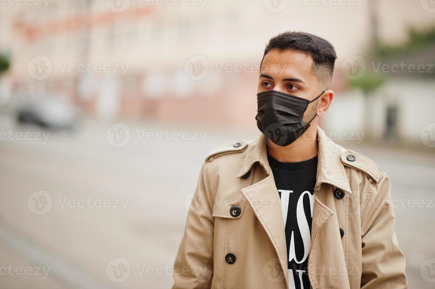 elegante kuwaiti uomo a trincea cappotto indossare nero viso maschera durante covid pandemismo. foto