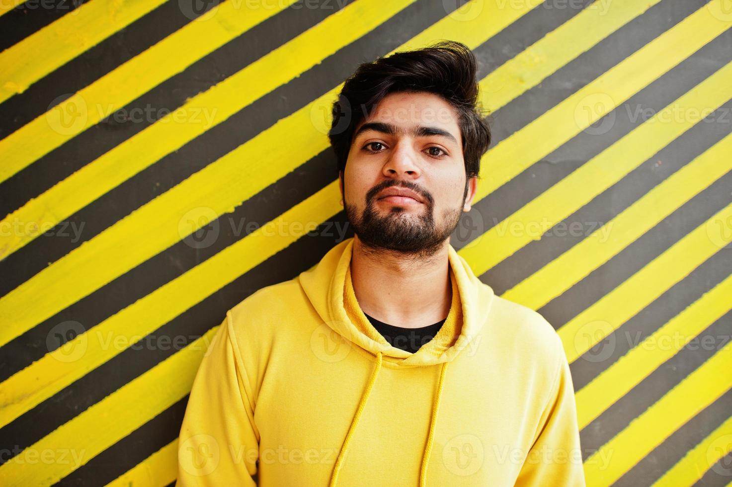 urbano giovane fricchettone indiano uomo nel un' alla moda giallo felpa. freddo Sud asiatico tipo indossare felpa con cappuccio contro a strisce sfondo. foto
