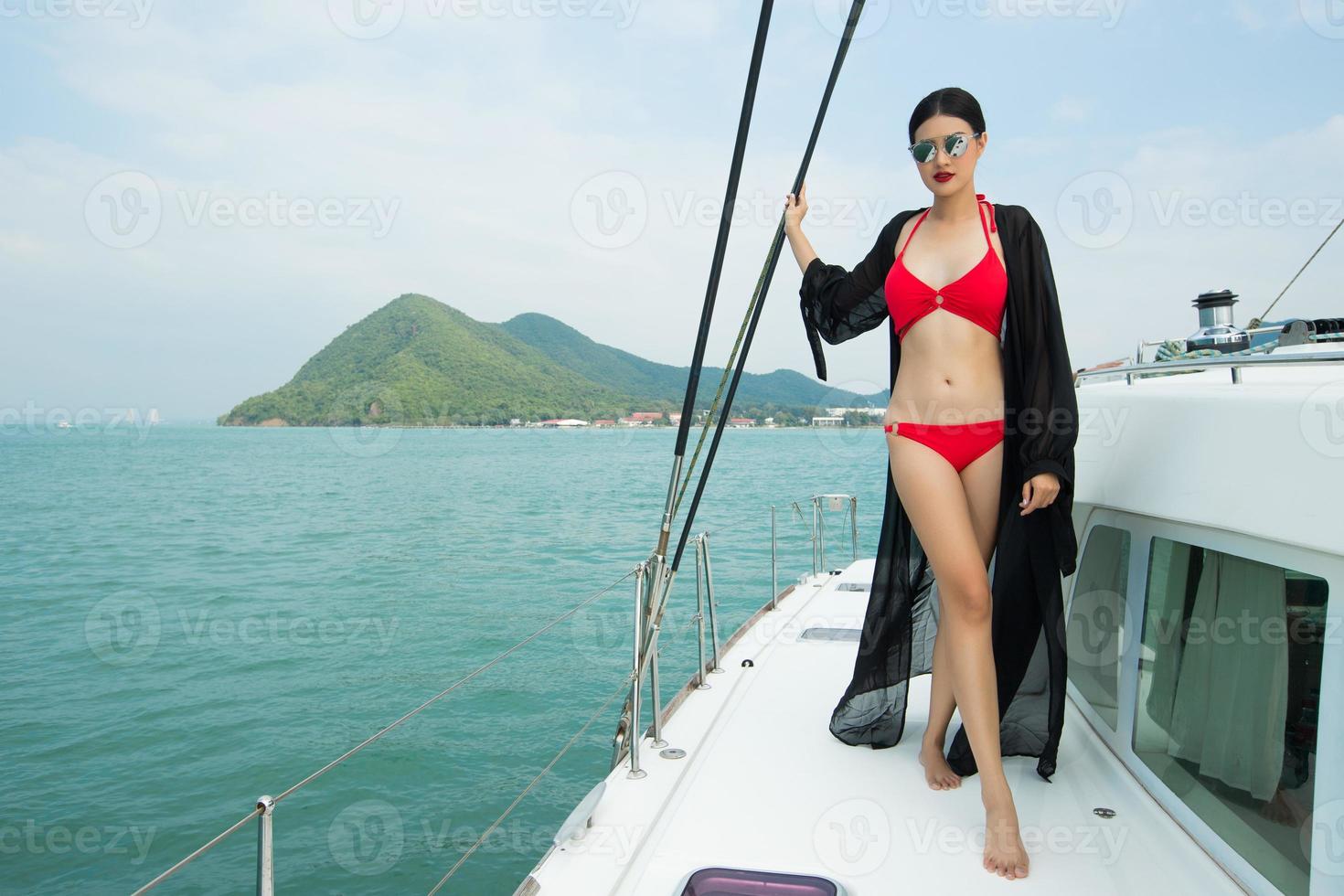 bellissimo asiatico mescolare gara abbronzato pelle donna camminare lungo lusso yachts nel in profondità oceano, rosso bikini occhiali da sole ragazza in posa come moda modello nel attracco molo sotto estate blu cielo nel vacanza vacanza foto