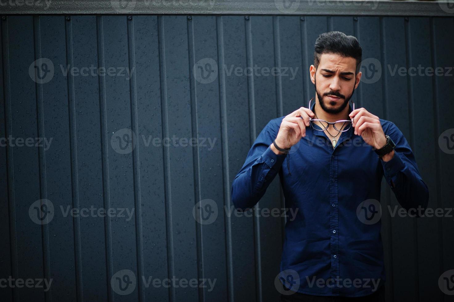 mezzo orientale imprenditore indossare blu camicia, occhiali, contro acciaio parete. foto