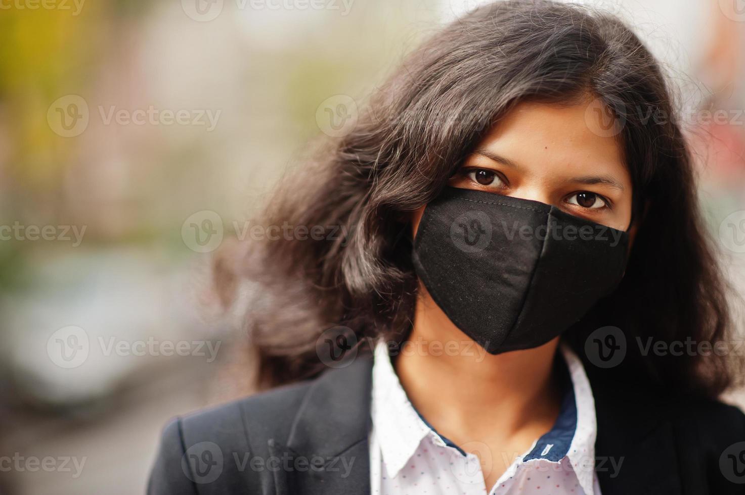 bellissima indiano donna indossare formale e nero viso maschera, in posa a strada durante covid pandemismo. foto