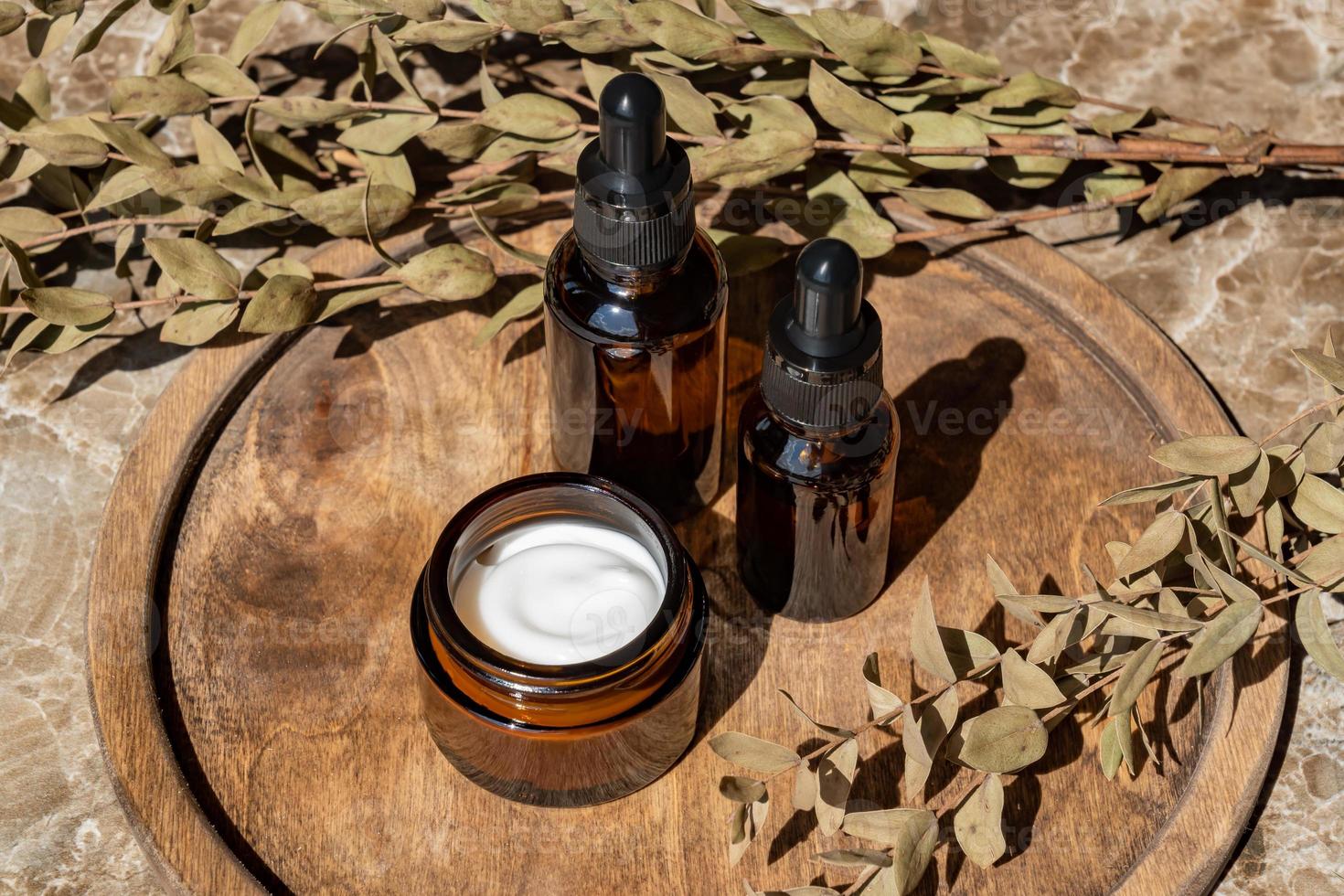 anti età collagene facciale siero nel buio bicchiere bottiglia e viso crema su di legno il giro vassoio con mazzo di asciutto eucalipto. naturale biologico cosmetico bellezza concetto. foto