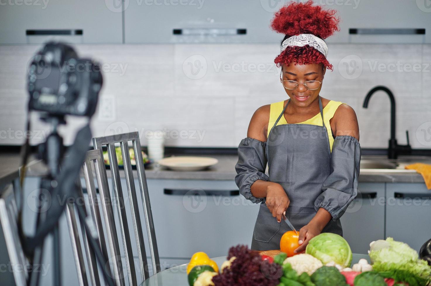 africano americano donna le riprese sua blog trasmissione di salutare cibo a casa cucina. lei tagli un' pomodoro con coltello. foto