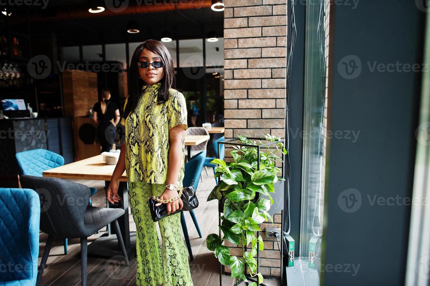 fascino africano americano donna indossare alla moda serpente vestito e occhiali da sole posa a ristorante. foto