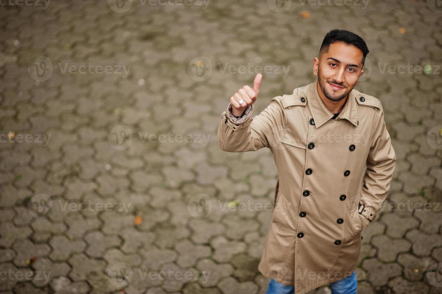 elegante kuwaiti uomo a trincea cappotto mostrare pollice su. foto