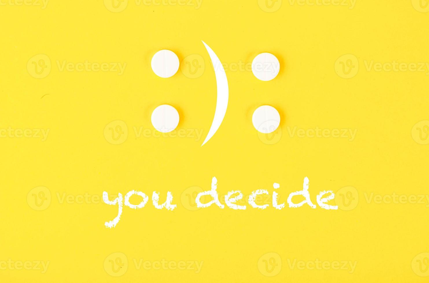 quattro bianca pillole nel il modulo di un' triste e allegro emoticon. il testo voi decidere. giallo sfondo. foto