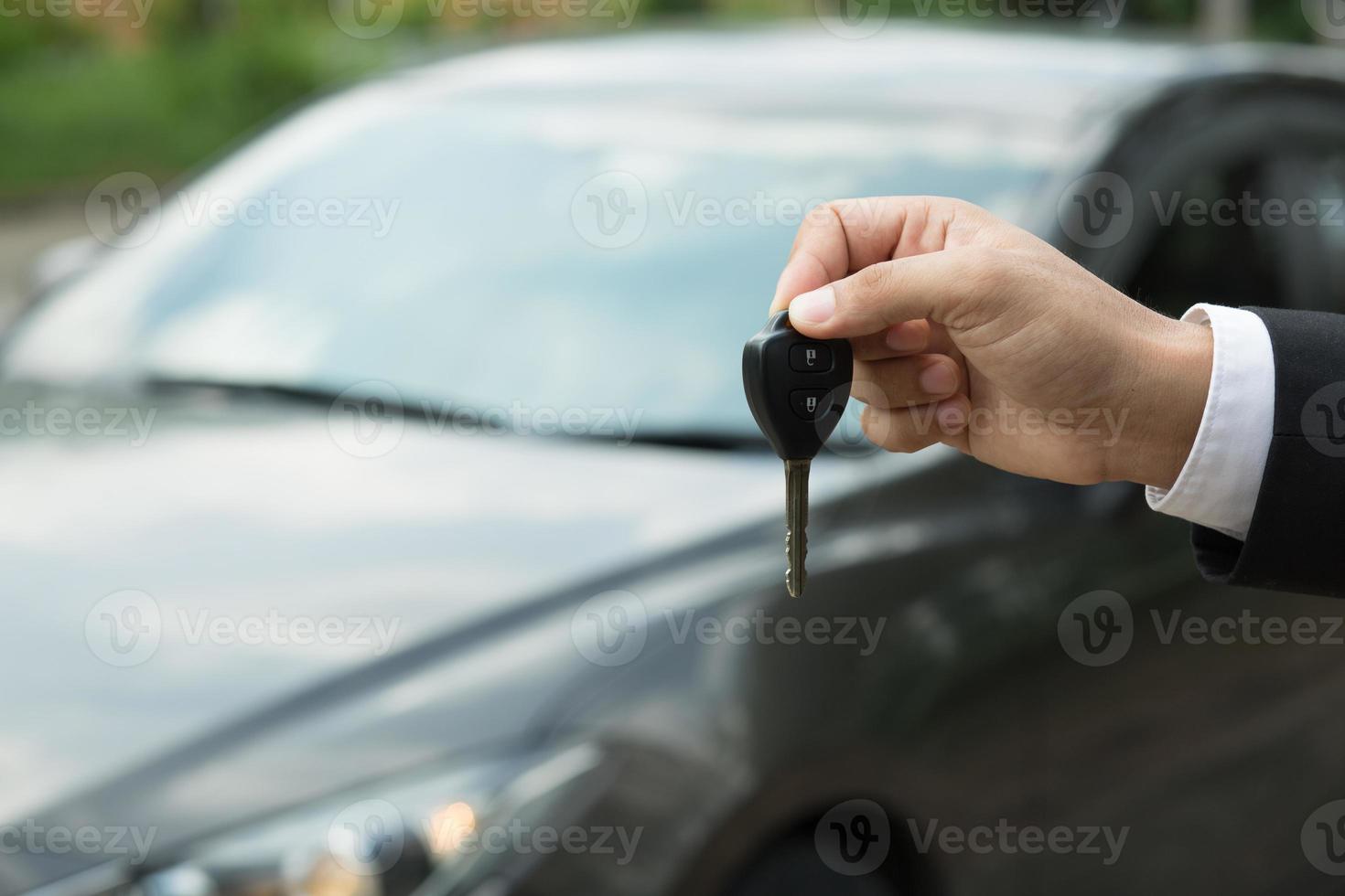 chiave dell'auto, l'uomo d'affari che consegna dà la chiave dell'auto all'altro uomo sullo sfondo dell'auto. foto