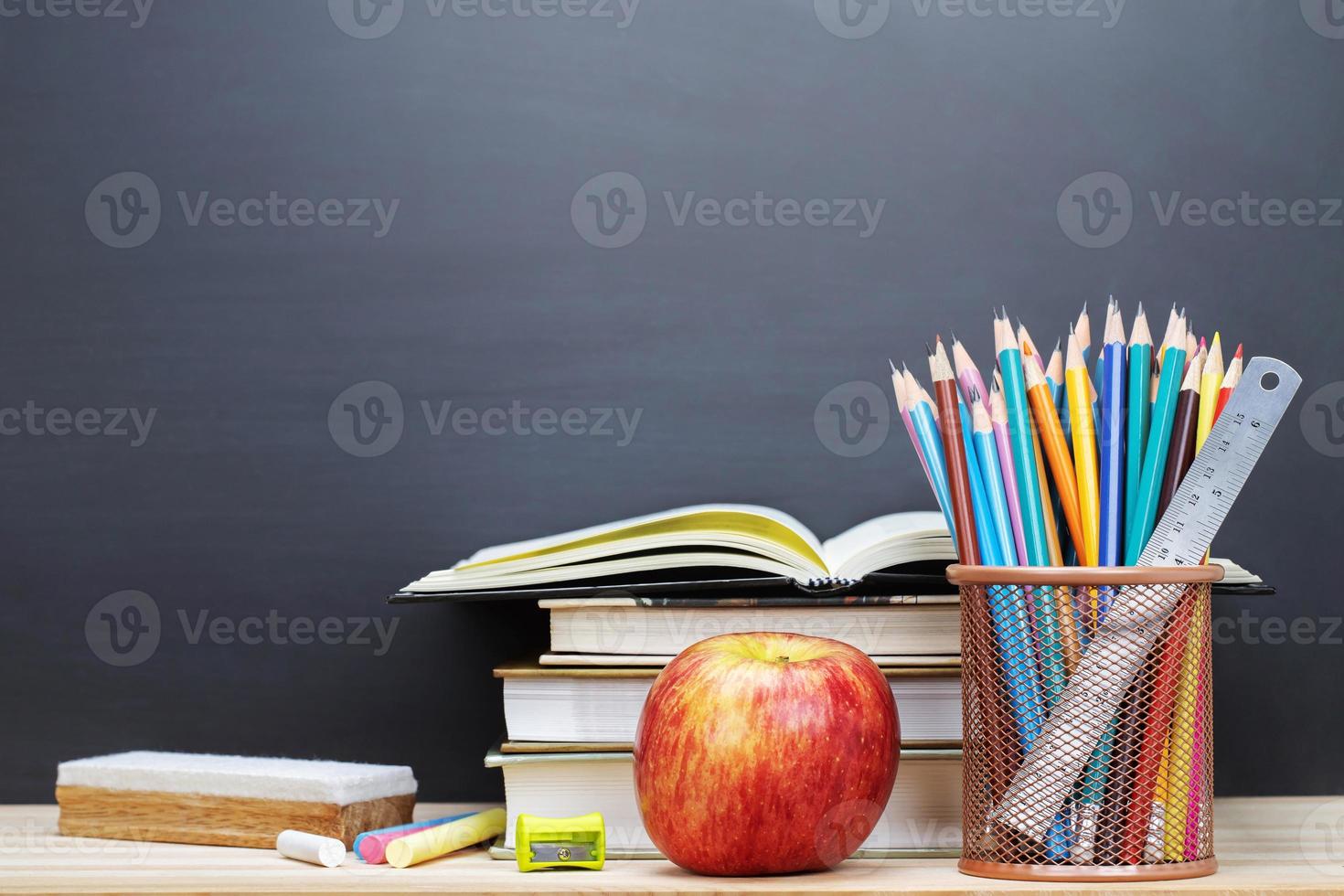 bicchieri insegnante libri e un' In piedi con matite su il tavolo, su il sfondo di un' lavagna con gesso. il concetto di il insegnanti giorno. foto