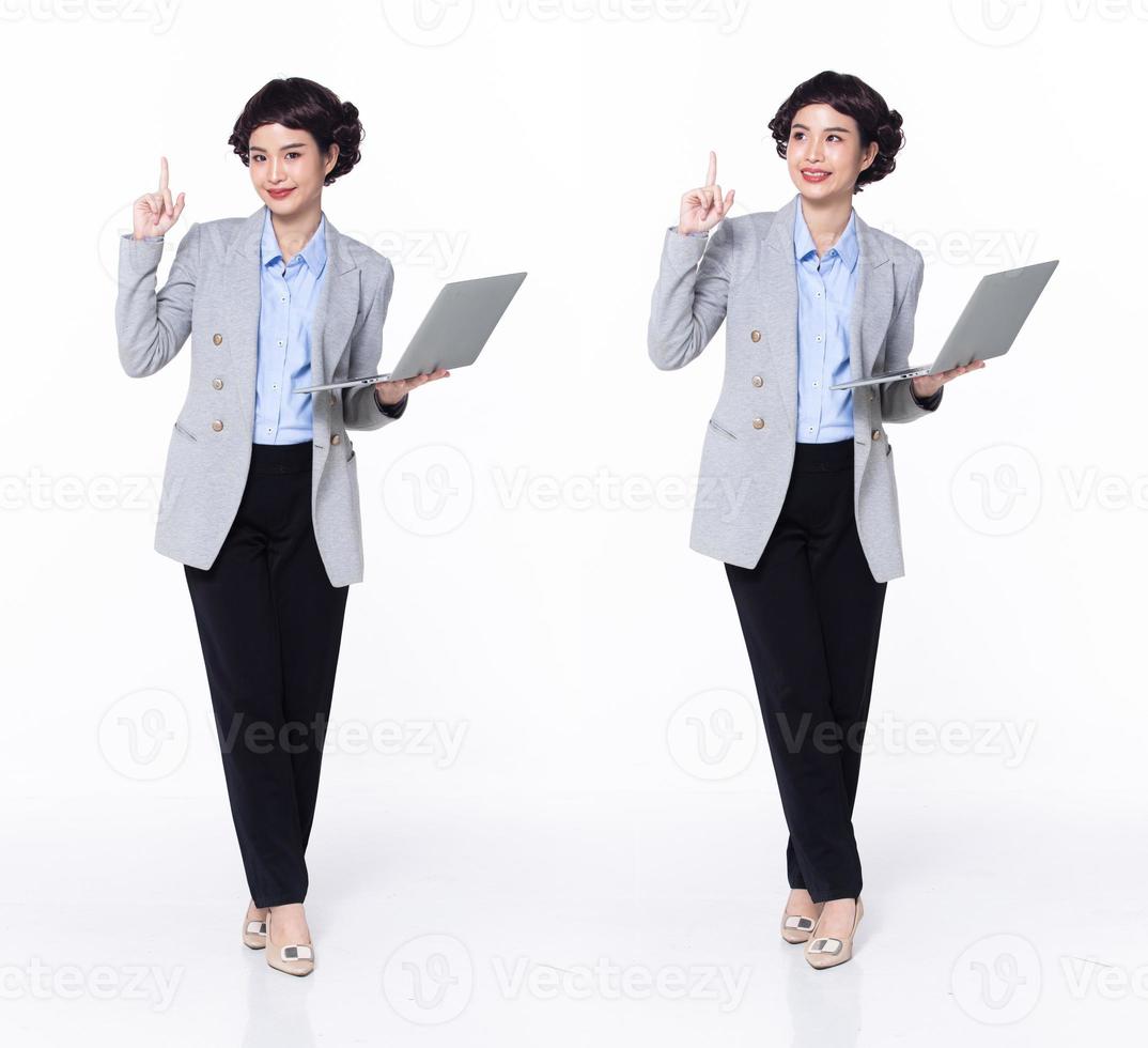 pieno lunghezza 30s anni 40 asiatico donna insegnante manager attività commerciale, puntamento dito su nel aria, indossare formale blazer pantaloni scarpe. Sorridi ufficio femmina trasportare il computer portatile caffè tazza al di sopra di bianca sfondo isolato foto