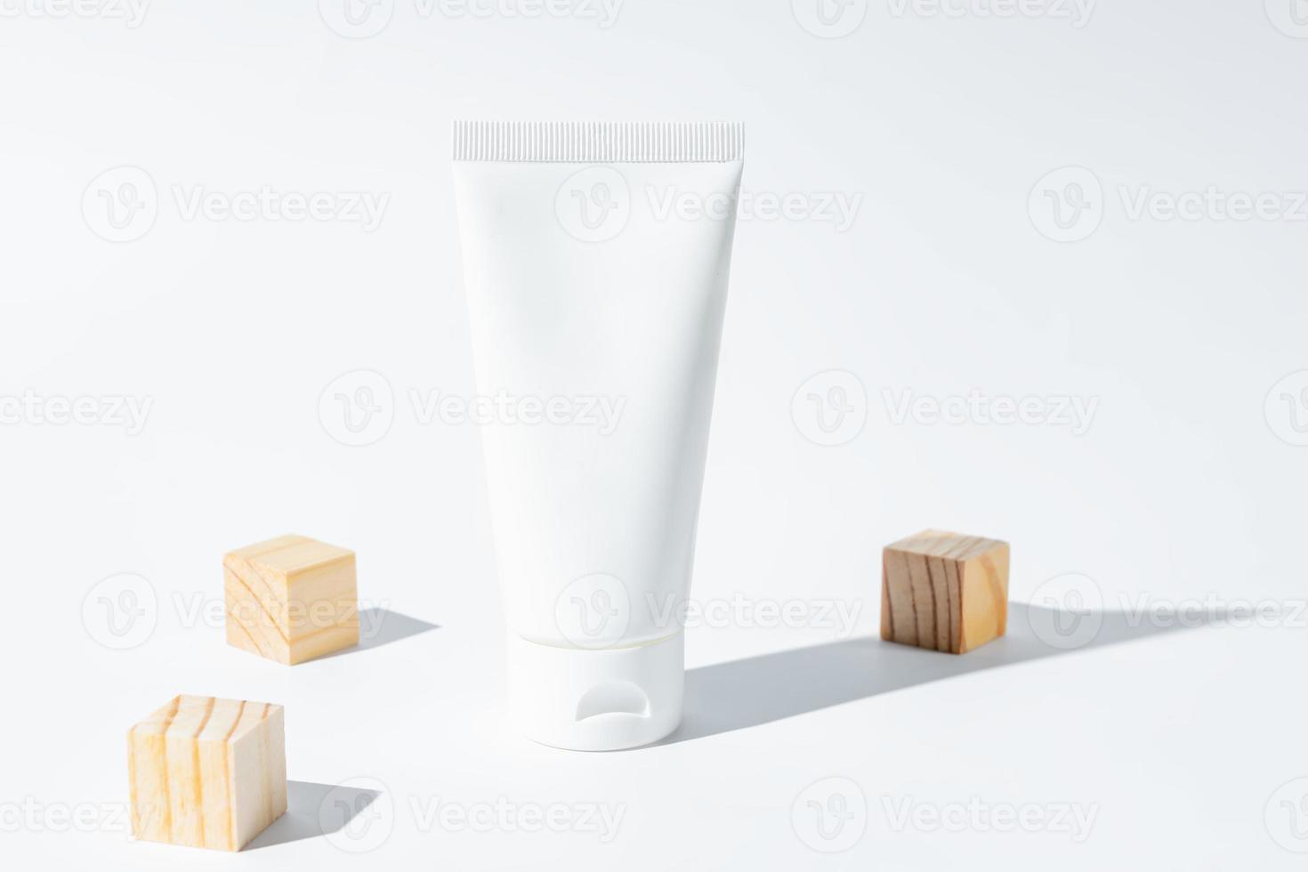 bellezza terme medico cosmetico lozione crema nel tubo bottiglia confezione su bianca sfondo con estate stagione sole leggero e sparpagliato di legno cubi foto